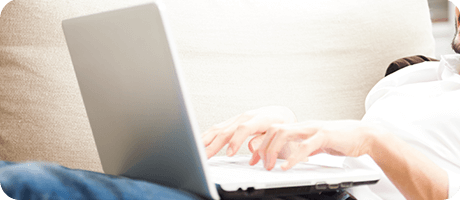 A person typing on a laptop while reclining on a couch, focused and relaxed.