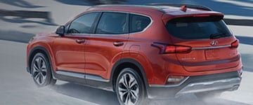 Red SUV driving on a snowy road, showcasing its winter performance and sleek design.