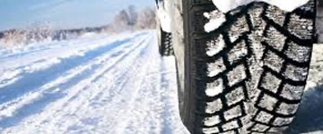 Close-up of a vehicle tire with snow-covered treads on a snowy road, indicating winter driving conditions.