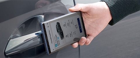 A person uses a smartphone app to unlock a car door, showcasing digital car key technology.