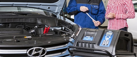 Mechanic discussing vehicle diagnostics with a customer beside an open Hyundai hood and testing equipment.