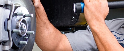 Mechanic inspecting car brake system using a flashlight.