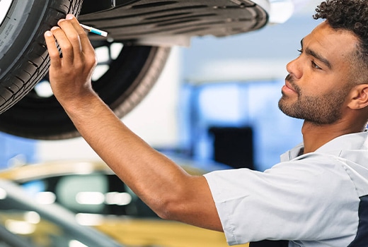 Mechanic inspecting a lifted car tire in an auto repair shop.