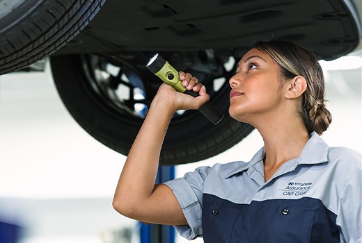 Mechanic in uniform inspecting car underside with flashlight at auto shop.