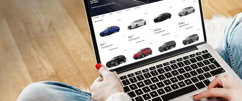 Person browsing a car dealership website on a laptop, displaying various vehicle models.