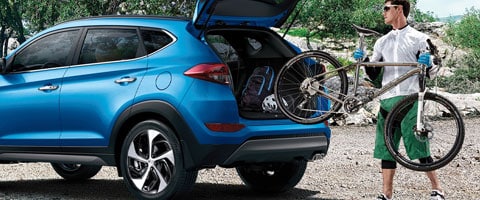 Man loading bicycle into a blue SUV's trunk, parked outdoors on a rocky terrain.