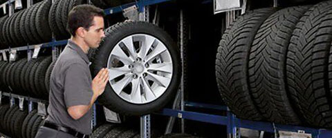 Man selecting a tire from a rack in an auto shop, surrounded by various tire options.