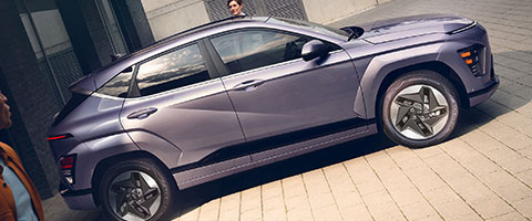 A sleek, modern purple SUV parked on a city street, with two people nearby, showcasing its stylish design.