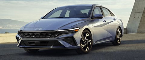 Silver sedan parked on a road with mountains in the background, under a clear sky.