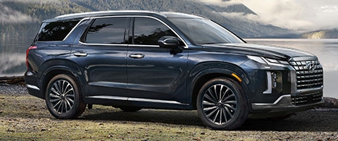 A sleek, black SUV parked by a serene lakeside with mountains in the background.