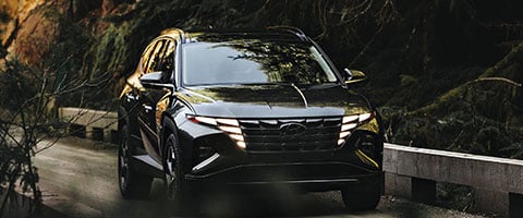 Black SUV driving through a forested area, highlighting its sleek design and headlights.