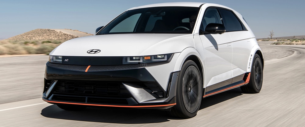 White Hyundai car driving on a desert road under a clear blue sky.