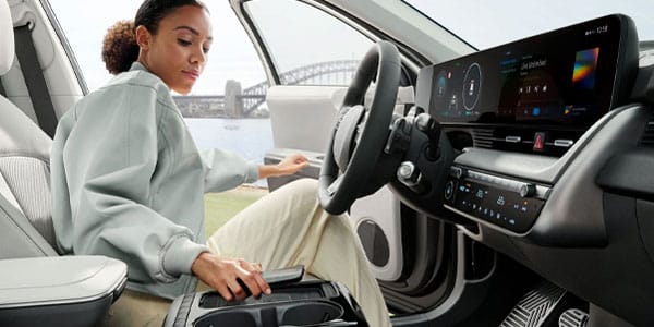 Woman inside a modern car with a digital dashboard, bridge visible outside the window.