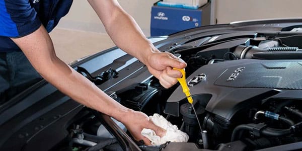 Mechanic checking engine oil with dipstick in a car's open hood. Car maintenance concept.