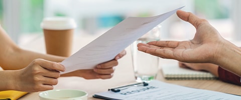 Two people exchange a resume during a job interview at a table with documents and drinks.
