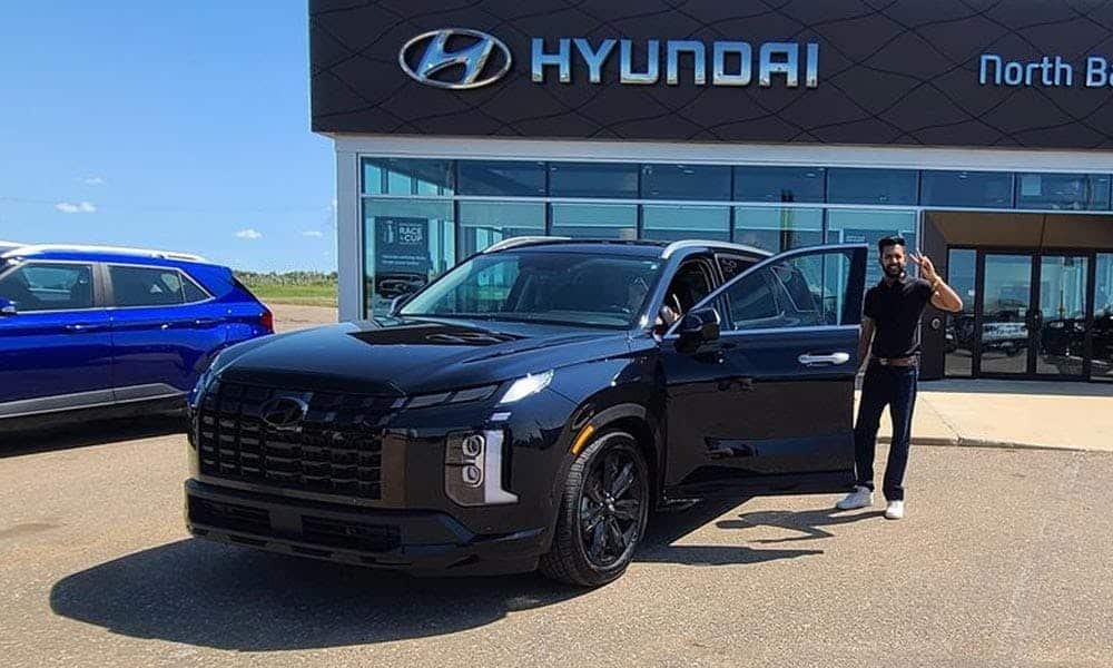 Man standing beside a black Hyundai SUV with an open door at a Hyundai dealership.