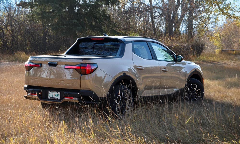 A silver pickup truck parked in a grassy field with trees in the background, under a clear sky.