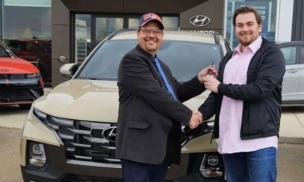 A happy customer receiving car keys from a salesperson in front of a new Hyundai SUV at a dealership.