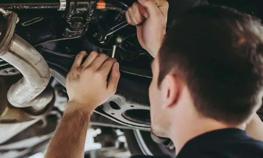 Mechanic inspecting and repairing a car's undercarriage, focusing on the exhaust system.