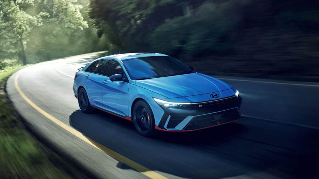 Blue Hyundai Elantra N driving on a winding road surrounded by lush green trees.