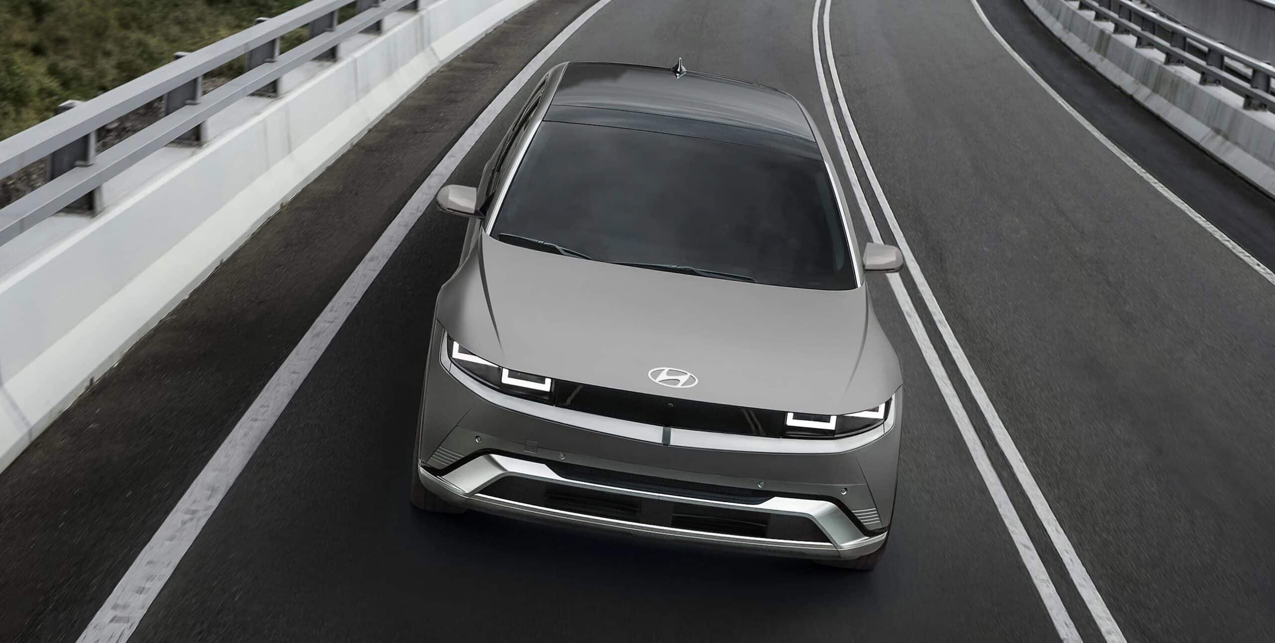 Silver Hyundai car driving on a highway, viewed from the front, with modern LED headlights.
