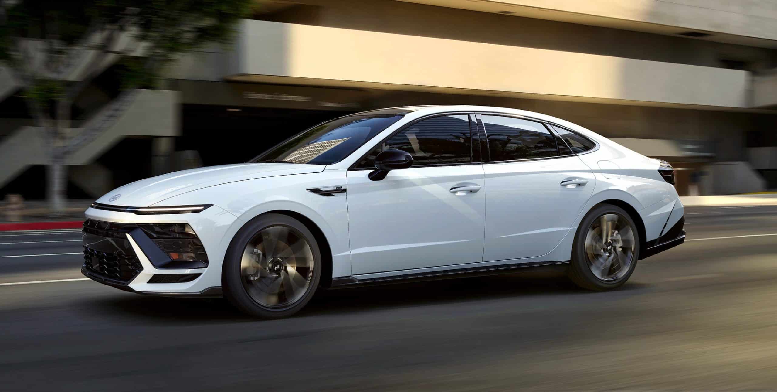 White sedan driving on an urban road, showcasing sleek design and aerodynamic features.