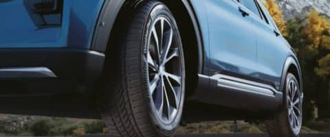 Blue SUV with alloy wheels on a scenic road, highlighting tire design and vehicle details.